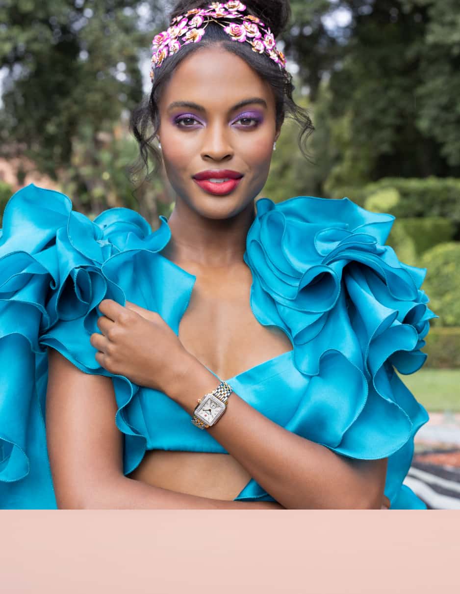 close up of woman wearing a two-piece turquoise ensemble and a MICHELE watch in the middle of a manicured garden