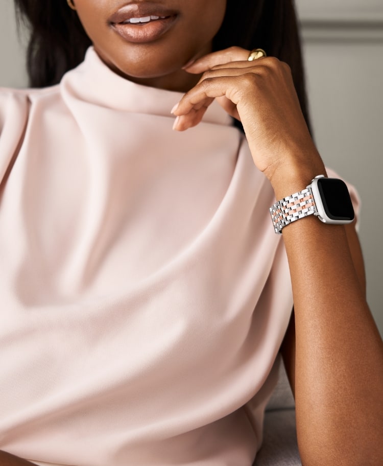 A woman in a light pink blouse wearing the two-tone 18K pink gold-plated bracelet band for Apple Watch®